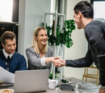 Two financial advisors having a meeting with young man at home. Female advisor is shaking hands with a client.